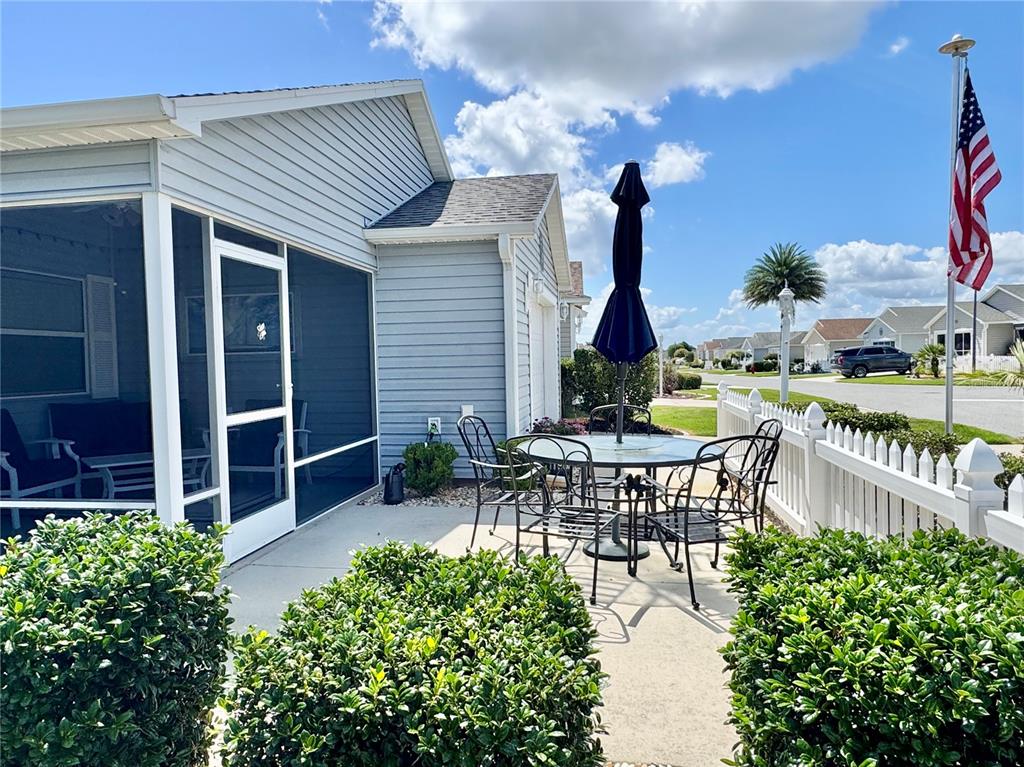 A patio with a dining set and umbrella sits beside a house with a screened porch — 1479 DYNASTY PLACE, THE VILLAGES, FL