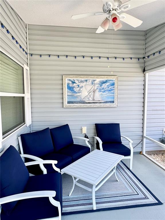 A screened-in porch features gray siding, navy blue patio furniture, and a sailboat wall art — 1479 DYNASTY PLACE, THE VILLAGES, FL