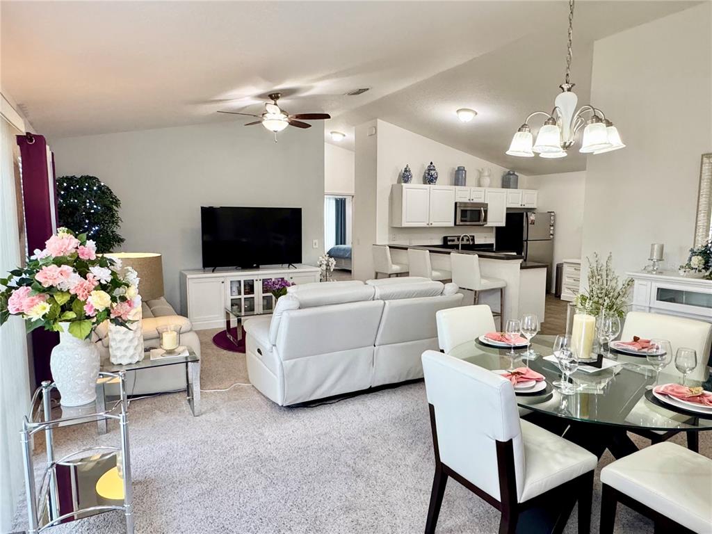 An open-concept living and dining area features white furniture, carpeted floors, and a kitchen island — 1479 DYNASTY PLACE, THE VILLAGES, FL