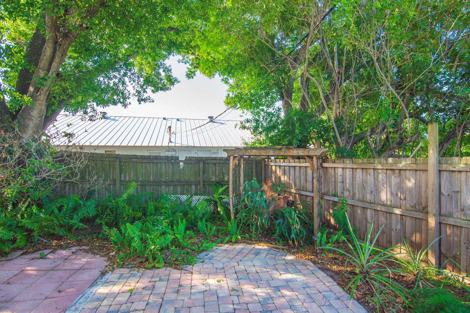 A backyard patio features a wooden pergola, lush green ferns, and a wooden privacy fence — 1545 Highland Avenue, Vero Beach FL 32960, VERO BEACH, FL