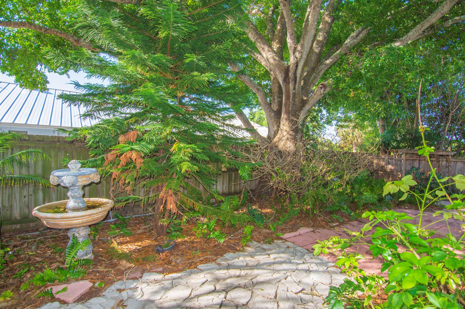 A backyard features a stone fountain, a large tree, and a paved stone walkway — 1545 Highland Avenue, Vero Beach FL 32960, VERO BEACH, FL
