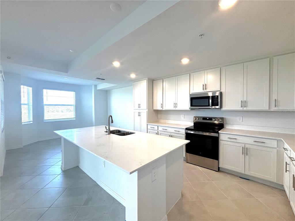 A modern kitchen features white cabinetry, a large quartz island, and stainless steel appliances — 17625 OPAL SAND DRIVE UNIT 202, VENICE, FL