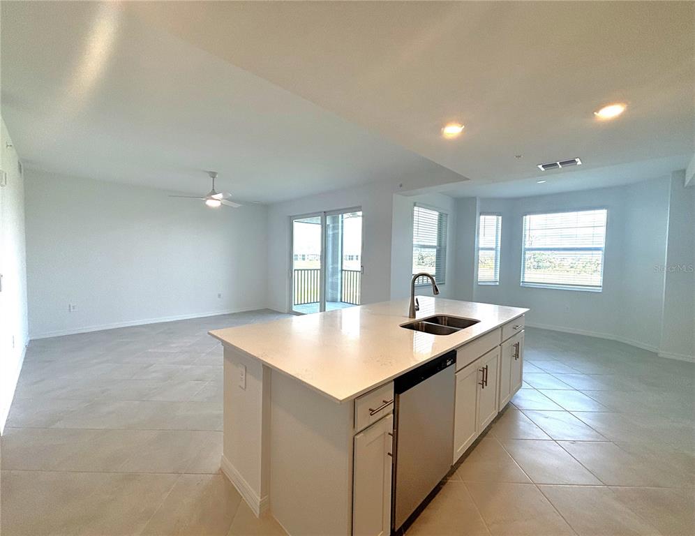 A kitchen island with a stainless steel dishwasher sits in an open-concept living area — 17625 OPAL SAND DRIVE UNIT 202, VENICE, FL