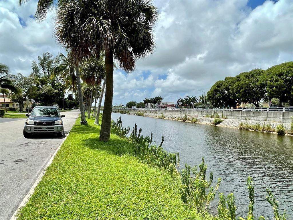 A dark car is parked on a grassy verge next to a canal and palm trees — 230 SW 1st Street # 8, Pompano Beach FL 33060, POMPANO BEACH, FL
