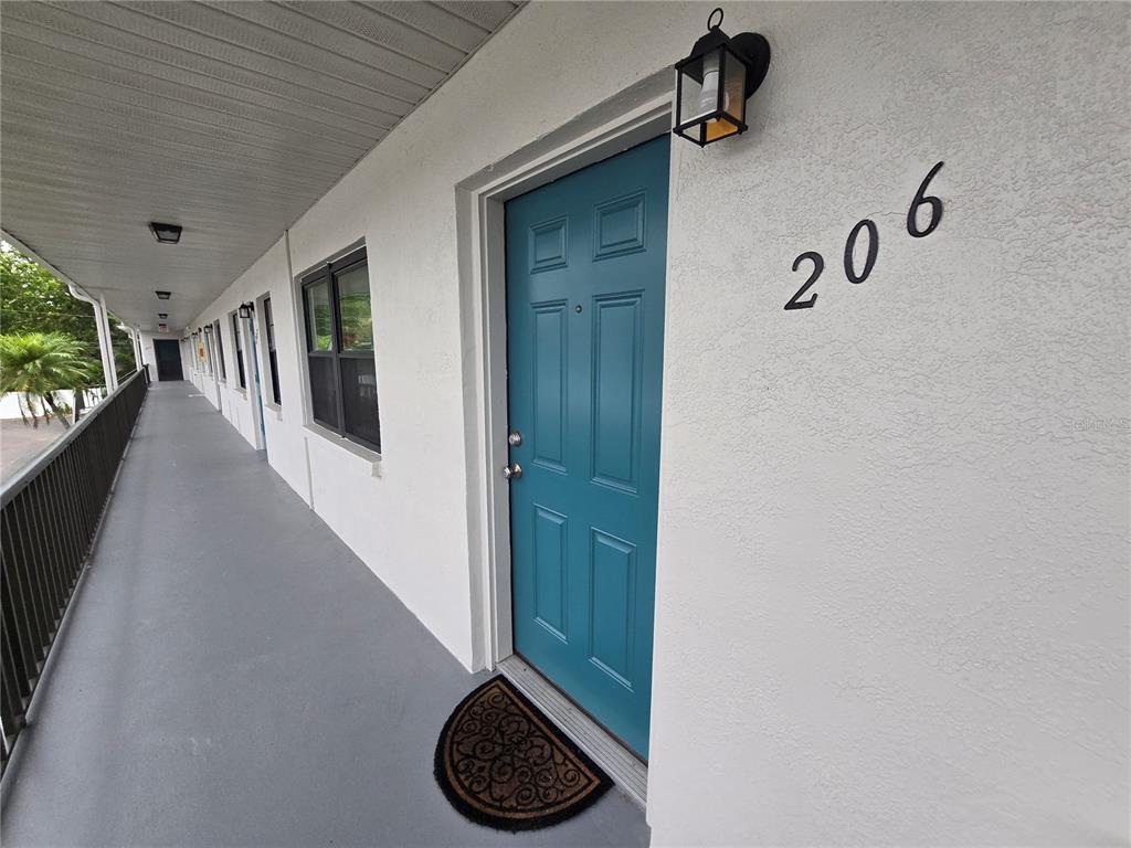 A teal front door with the number 206 is located on an outdoor apartment walkway — 5967 TERRACE PARK DRIVE N UNIT 206, ST PETERSBURG, FL
