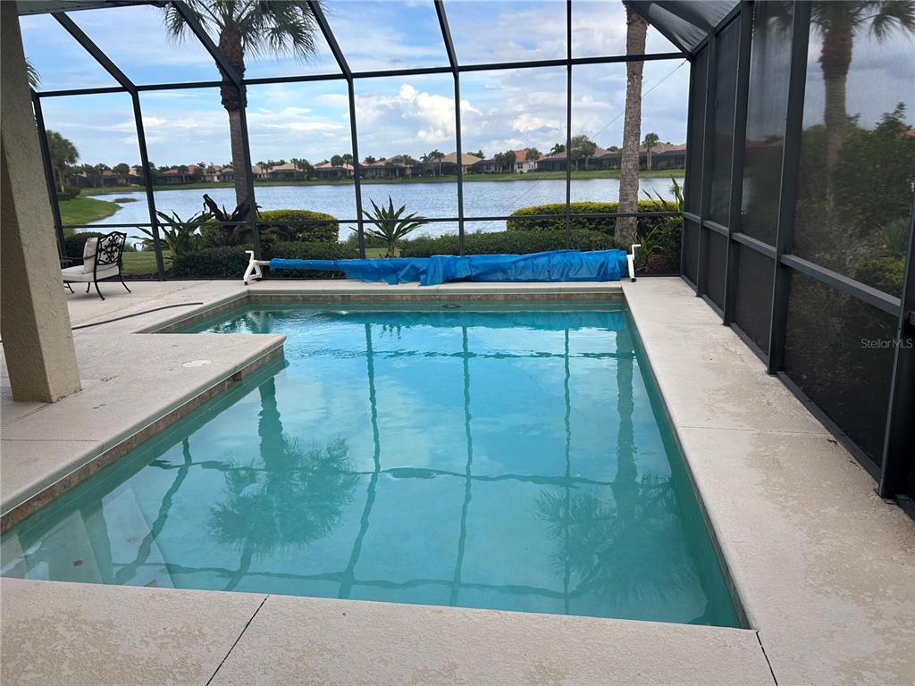 A screened-in swimming pool overlooks a lake with palm trees and residential homes — 110 CANELETTO WAY, NORTH VENICE, FL