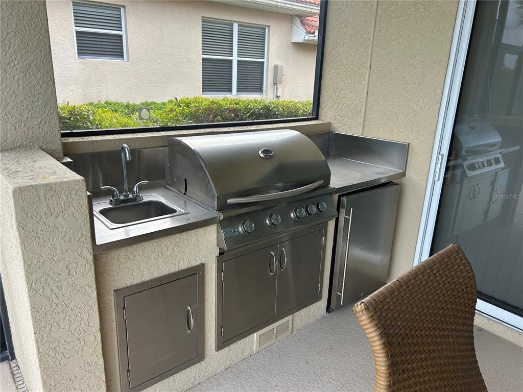 An outdoor kitchen features a stainless steel grill, sink, and cabinetry on a covered patio — 110 CANELETTO WAY, NORTH VENICE, FL