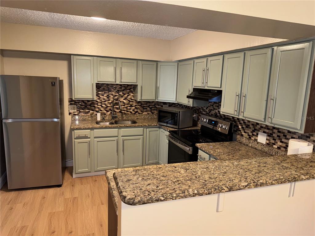 A kitchen features light green cabinets, granite countertops, a mosaic tile backsplash, and stainless appliances — 613 CAROL TER UNIT Main, KISSIMMEE, FL
