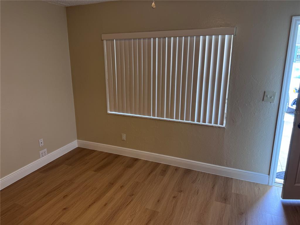 An empty room features light brown wood-look flooring, beige walls, and a window with vertical blinds — 613 CAROL TER UNIT Main, KISSIMMEE, FL