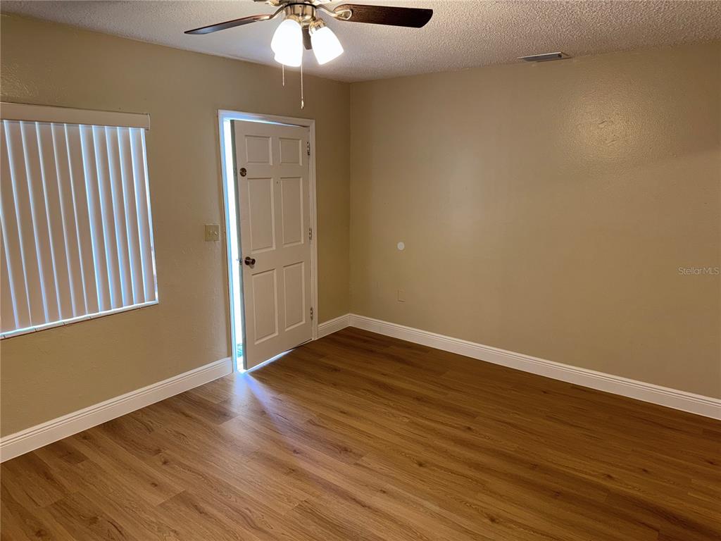 An empty room features wood-look flooring, beige walls, a ceiling fan, and an open door — 613 CAROL TER UNIT Main, KISSIMMEE, FL