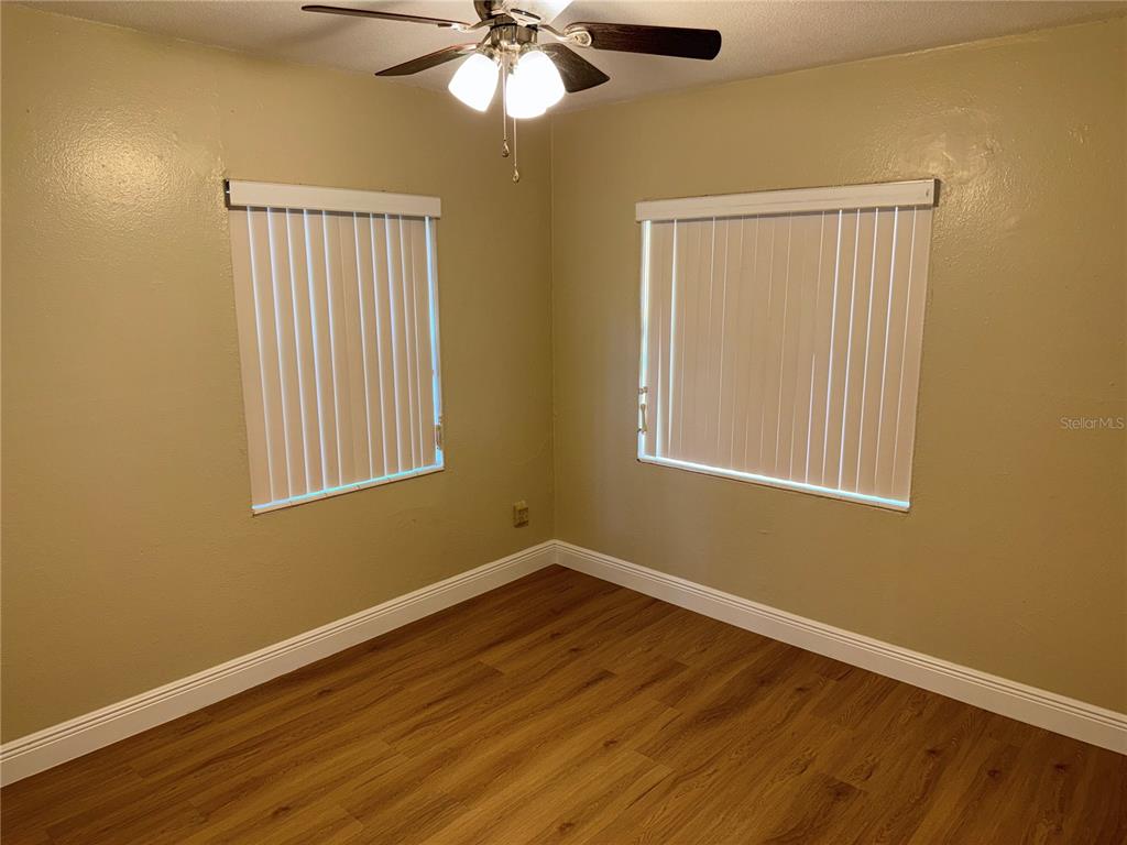 An empty bedroom features tan walls, wood-look flooring, and two windows with white blinds — 613 CAROL TER UNIT Main, KISSIMMEE, FL