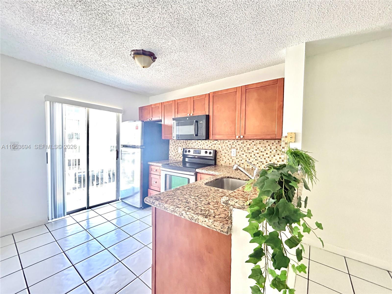 A kitchen features wood cabinets, granite countertops, a stainless steel refrigerator, and tiled flooring — 2575 SW 27th Ave # 509, Miami FL 33133, MIAMI, FL