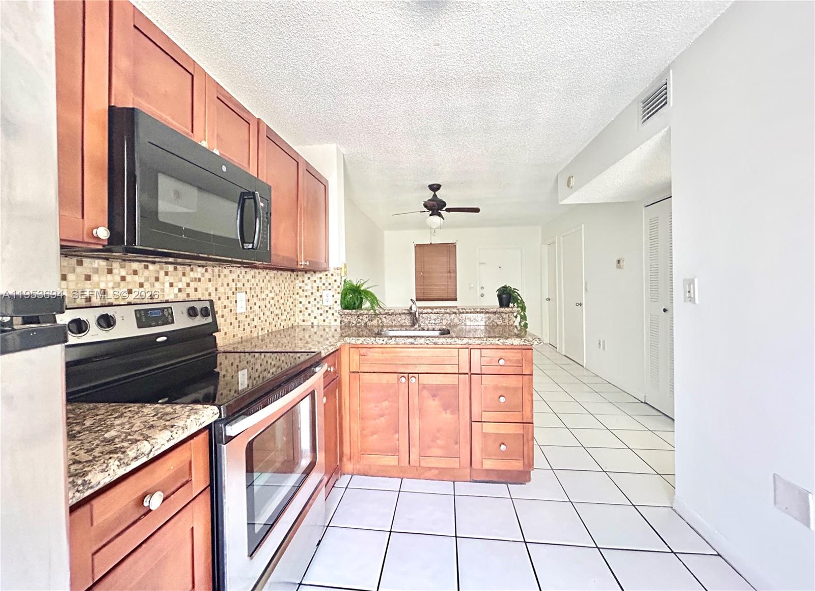 A kitchen features wood cabinets, granite countertops, a black microwave, and white tile flooring — 2575 SW 27th Ave # 509, Miami FL 33133, MIAMI, FL