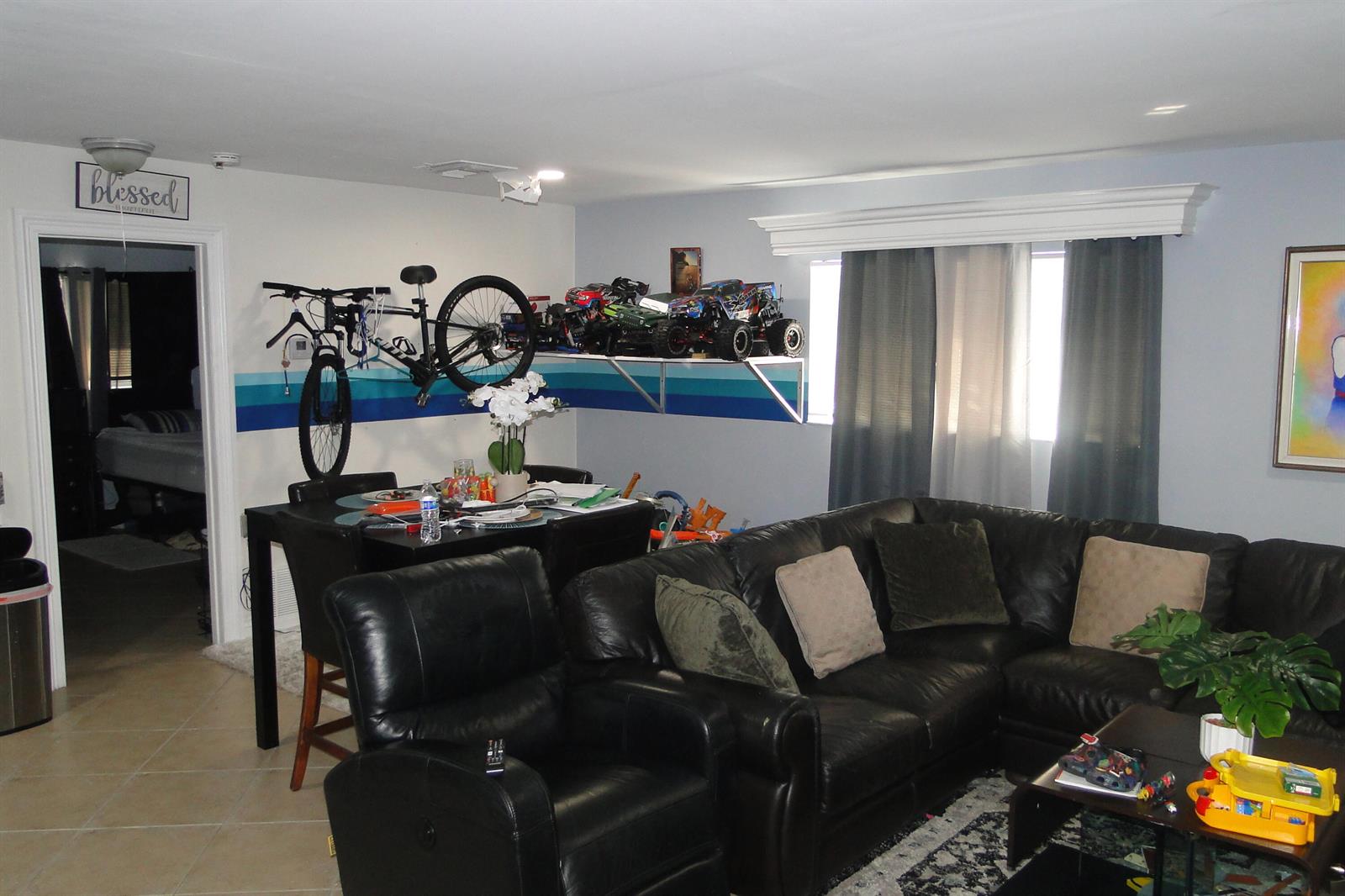 A living room features a black leather sectional, a dining table, and wall-mounted toy trucks — 1829 N A Street # 14, FL 33460, FL