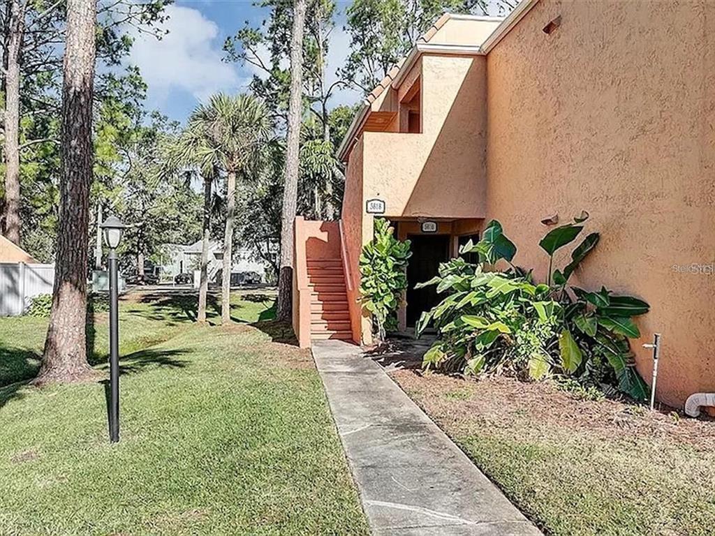 A tan stucco building exterior features an outdoor staircase, a walkway, and lush green landscaping — 5818 WINDHOVER DRIVE UNIT 5818, ORLANDO, FL