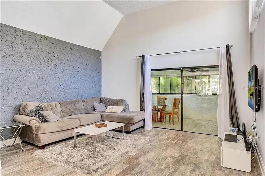 A living room features a textured gray accent wall, vaulted ceilings, and sliding glass doors — 5818 WINDHOVER DRIVE UNIT 5818, ORLANDO, FL