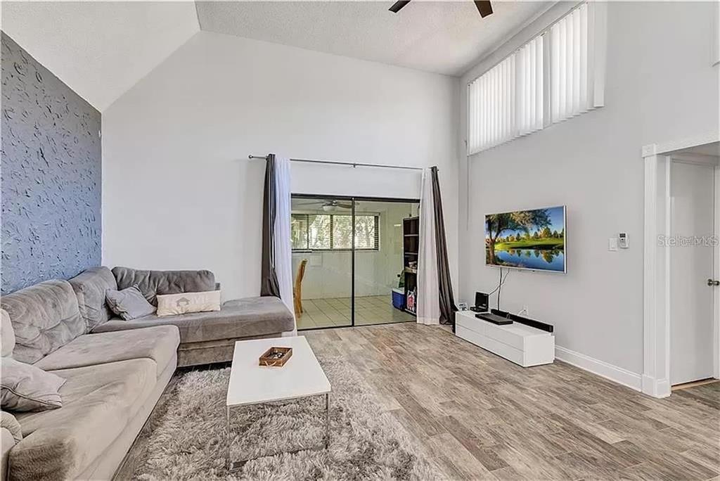 A living room with vaulted ceilings, gray wood-look flooring, a sectional sofa, and a television — 5818 WINDHOVER DRIVE UNIT 5818, ORLANDO, FL