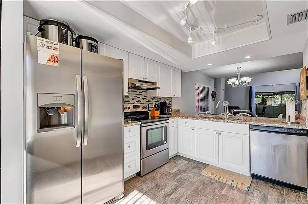 A kitchen with stainless steel appliances, white cabinets, granite countertops, and wood-look flooring — 5818 WINDHOVER DRIVE UNIT 5818, ORLANDO, FL