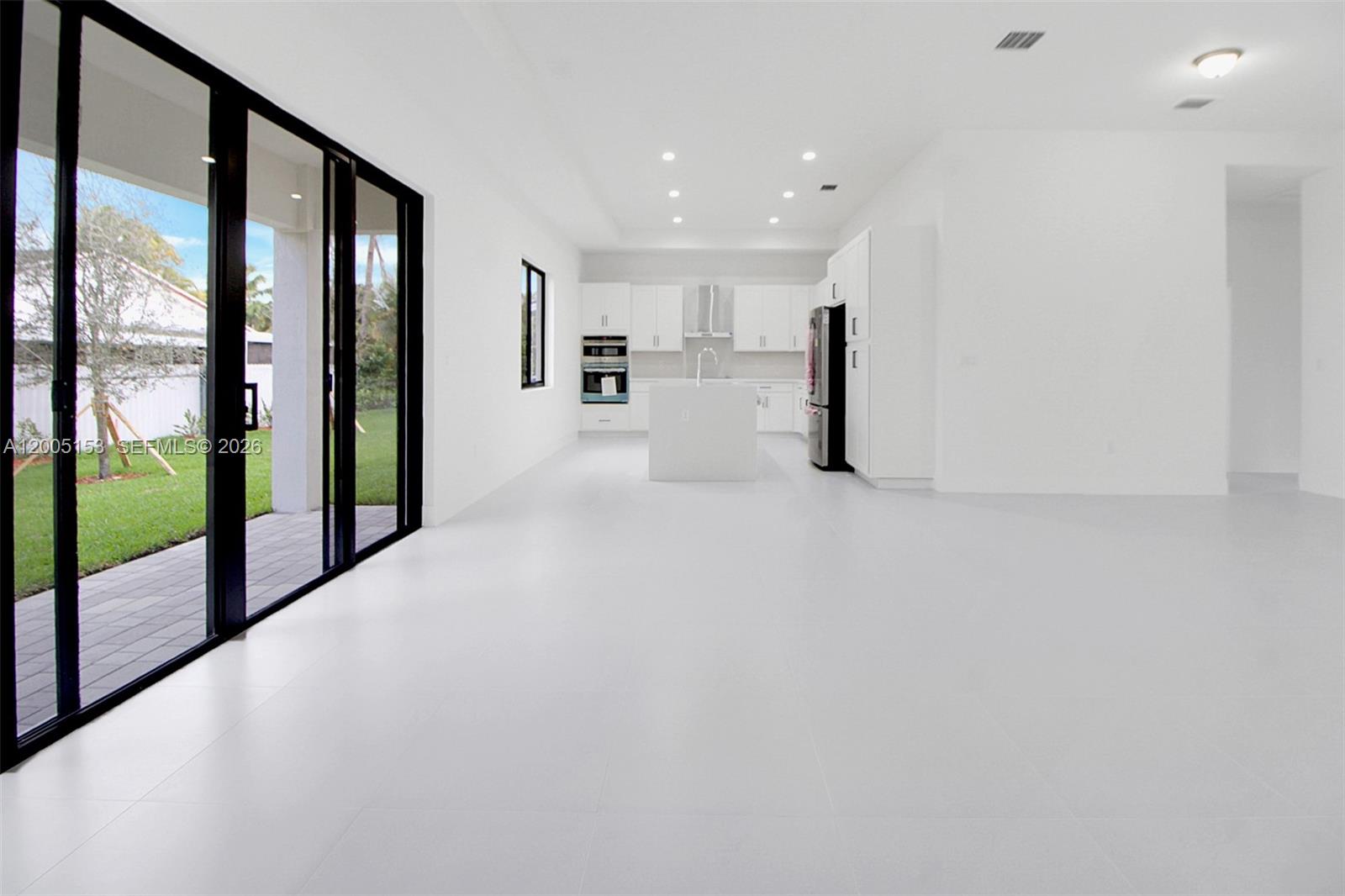 A modern, minimalist kitchen features white cabinetry, a center island, and large sliding glass doors — 20833 SW 96th Ct, Cutler Bay FL 33189, CUTLER BAY, FL