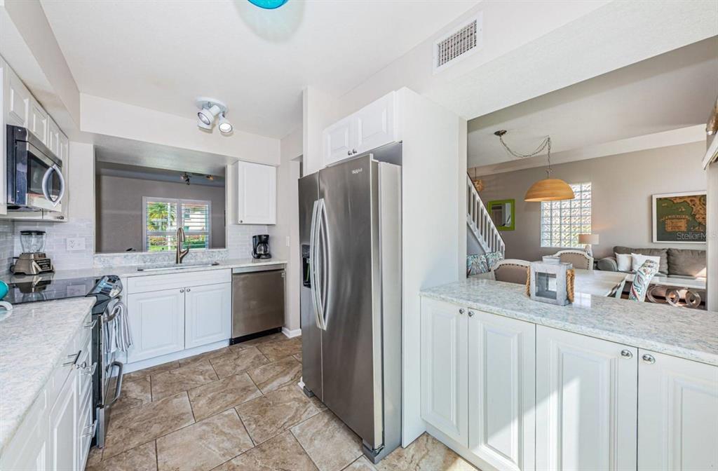 A kitchen with white cabinets, stainless steel appliances, and light countertops opens to a dining area — 6107 MIRADA CIRCLE, ST PETERSBURG, FL