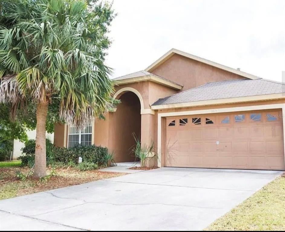A single-story house with a tan stucco exterior, a palm tree, and a two-car garage — 2697 AUTUMN CREEK CIRCLE, KISSIMMEE, FL