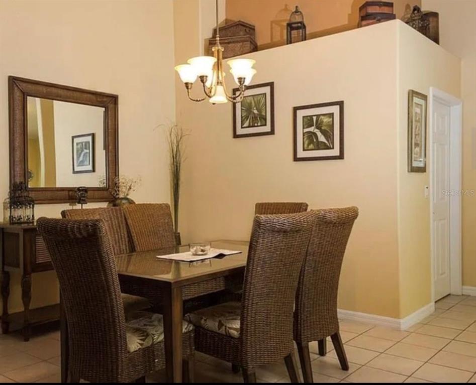 A dining room features a glass-topped table, wicker chairs, a chandelier, and framed wall art — 2697 AUTUMN CREEK CIRCLE, KISSIMMEE, FL