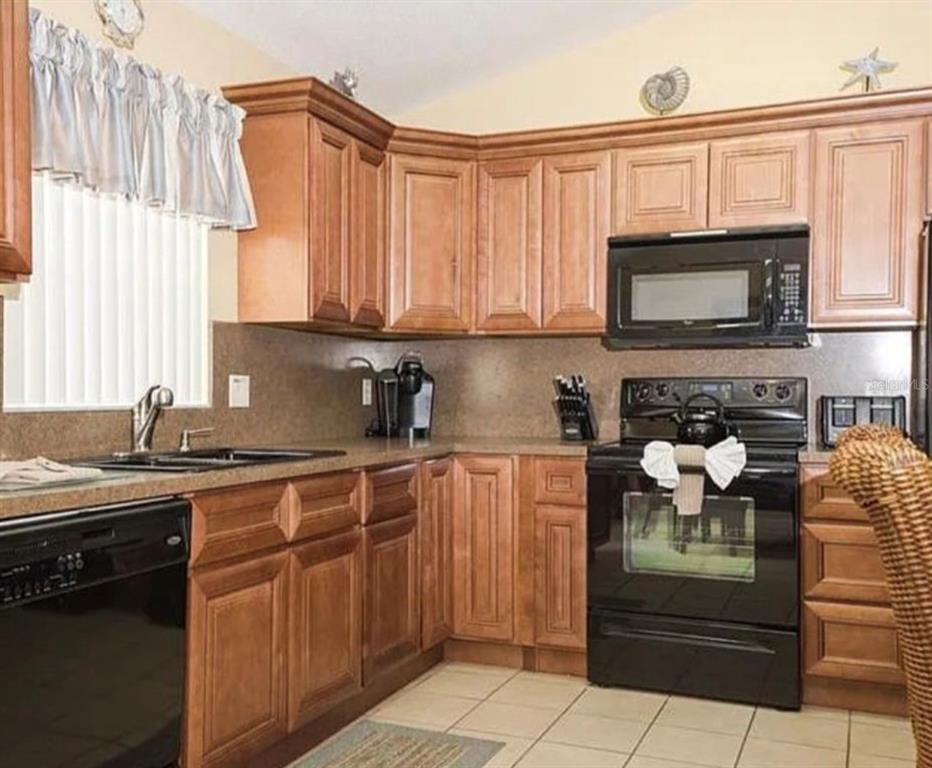 A kitchen features wood cabinets, black appliances, a double sink, and light-colored tile flooring — 2697 AUTUMN CREEK CIRCLE, KISSIMMEE, FL