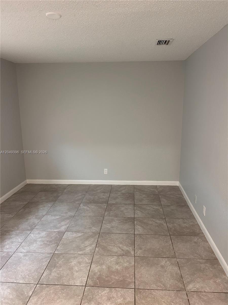 An empty room features gray walls, a textured white ceiling, and brown tiled flooring — 1530 S Congress Ave # 2, Delray Beach FL 33445, DELRAY BEACH, FL