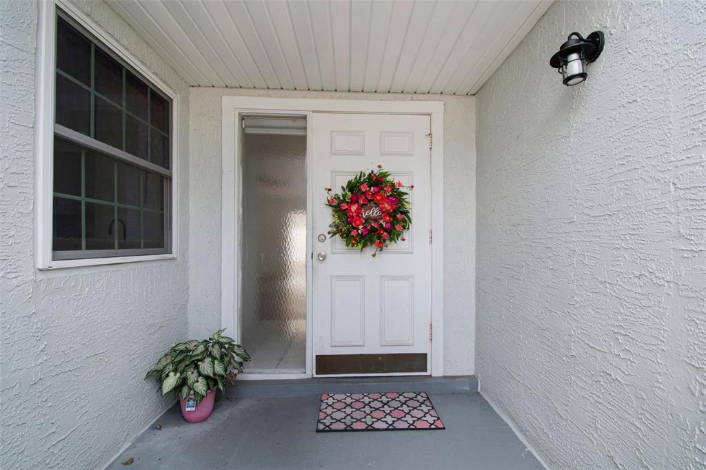 A white front door with a floral wreath and side window sits on a porch — 341 HIBISCUS DRIVE, PALM HARBOR, FL