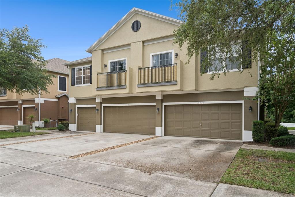 A two-story townhouse exterior features three garage doors, two balconies, and a concrete driveway — 15316 OAK APPLE COURT UNIT B, WINTER GARDEN, FL