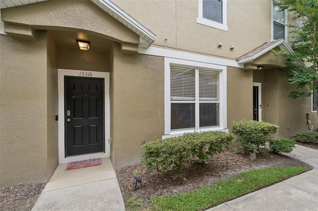 The exterior of a tan townhouse features a black front door and a large window — 15316 OAK APPLE COURT UNIT B, WINTER GARDEN, FL