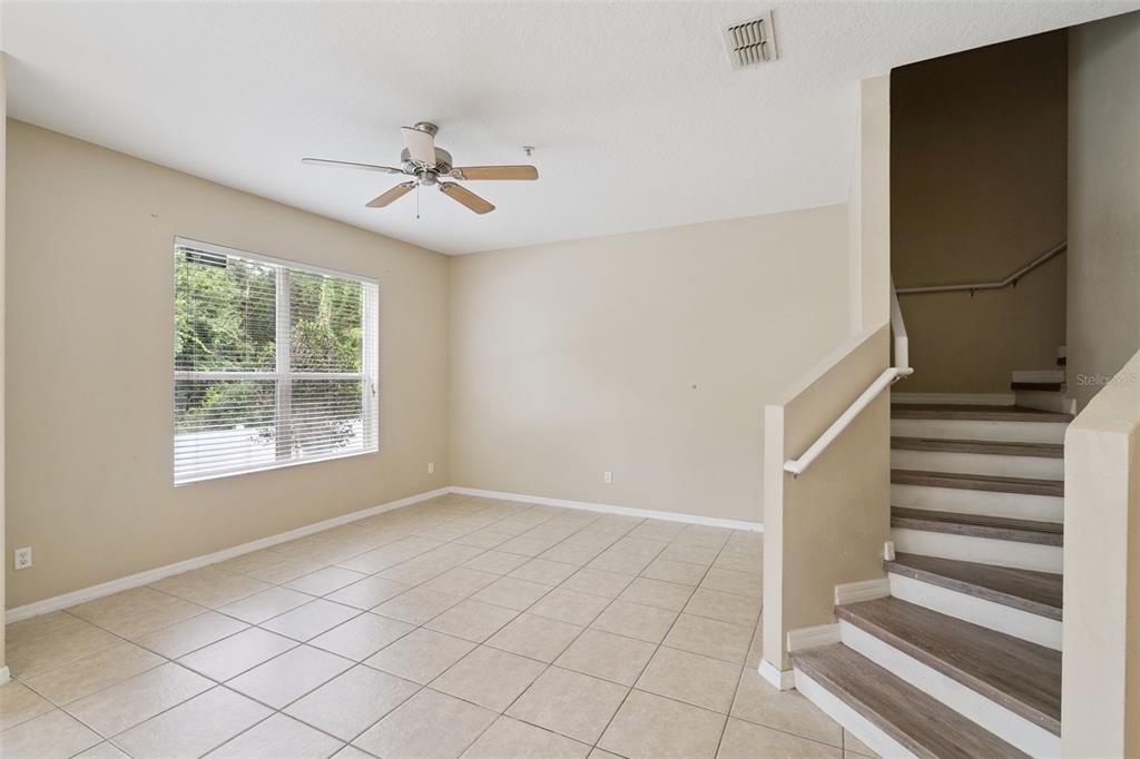 An empty living room features beige walls, tile flooring, a ceiling fan, and a staircase — 15316 OAK APPLE COURT UNIT B, WINTER GARDEN, FL