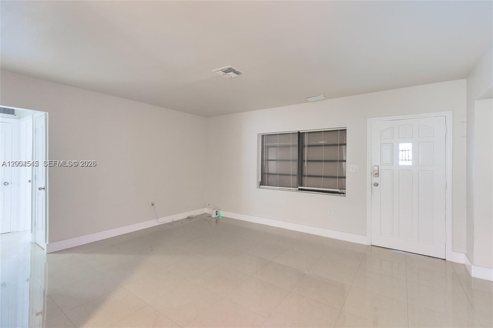 An empty room features light-colored tile flooring, white walls, a window with blinds, and a door — 14601 NW 10th Ave # 1, Miami FL 33168, MIAMI, FL