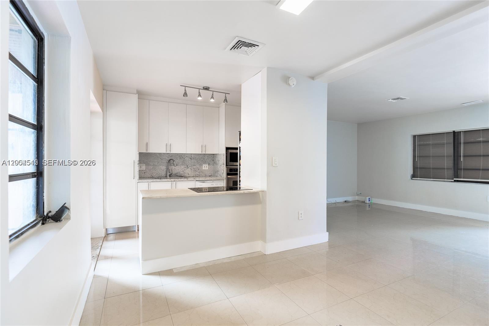 A kitchen with white cabinets and a breakfast bar opens into a tiled living area — 14601 NW 10th Ave # 1, Miami FL 33168, MIAMI, FL