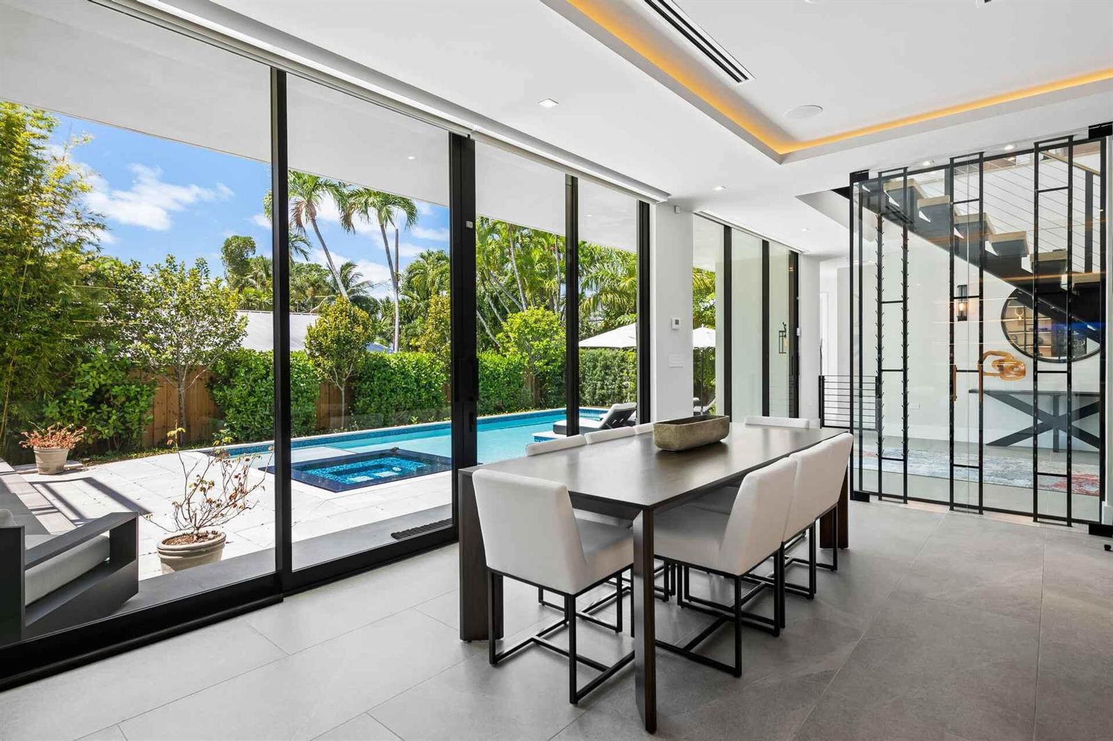 A modern dining room with a dark table, white chairs, and floor-to-ceiling windows overlooking a pool — 5288 Alton Road # 2, Miami Beach FL 33140, MIAMI BEACH, FL