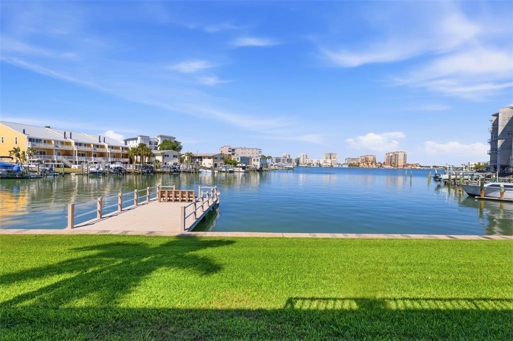 A grassy lawn overlooks a boat dock and a calm bay with distant buildings — 400 LARBOARD WAY UNIT 105, CLEARWATER BEACH, FL