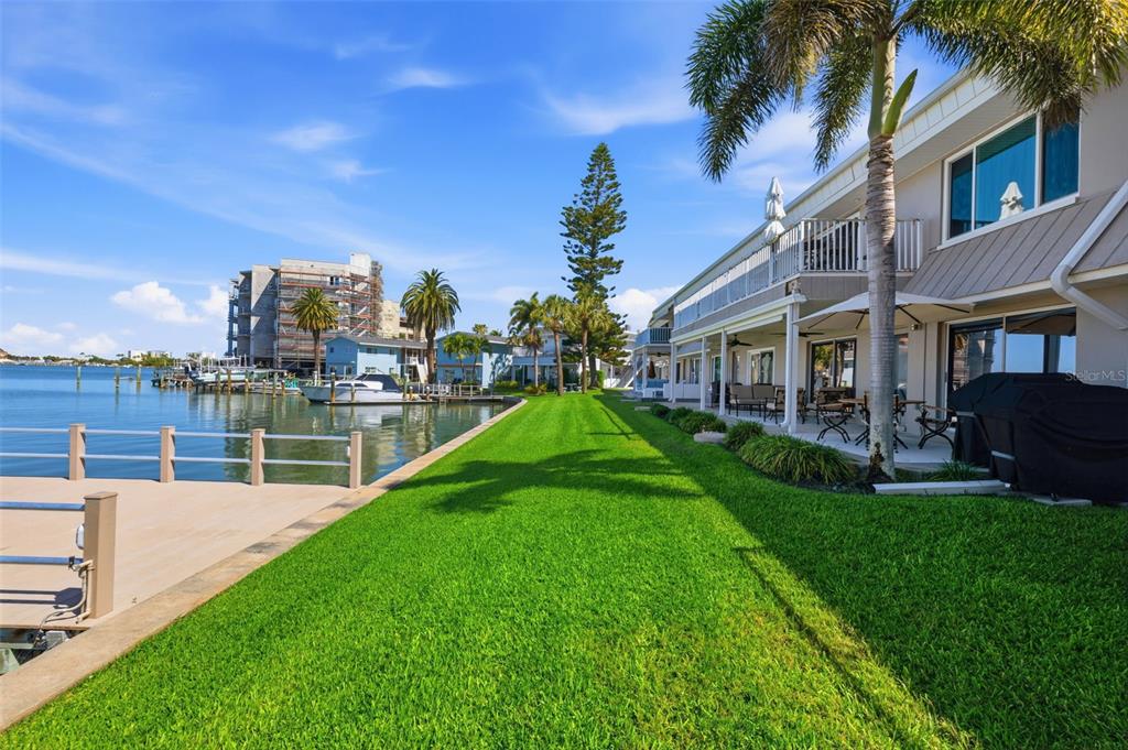 A waterfront property features a green lawn, a wooden dock, and a multi-story building — 400 LARBOARD WAY UNIT 105, CLEARWATER BEACH, FL