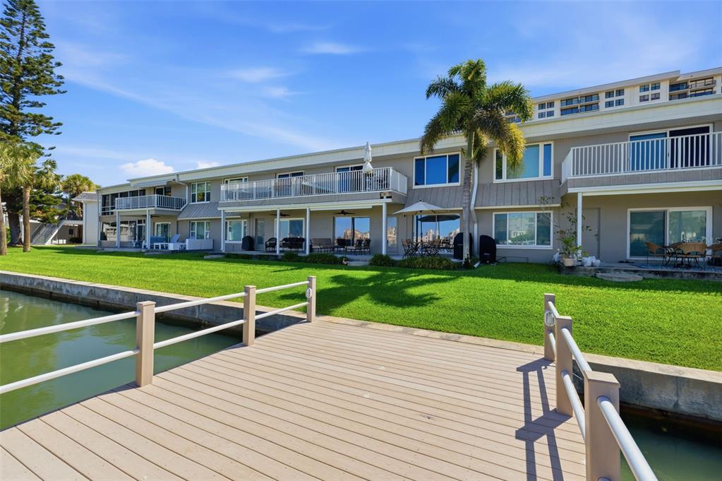 A wooden dock overlooks a grassy lawn and the rear exterior of a multi-story building — 400 LARBOARD WAY UNIT 105, CLEARWATER BEACH, FL