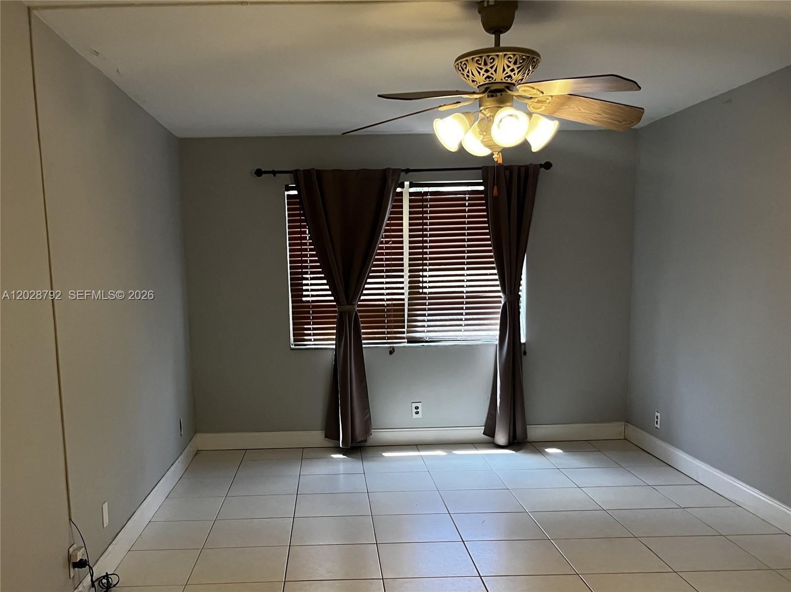 An empty room features gray walls, light-colored tile flooring, a ceiling fan, and a window — 7000 Nova Dr # 103E, Davie FL 33317, DAVIE, FL