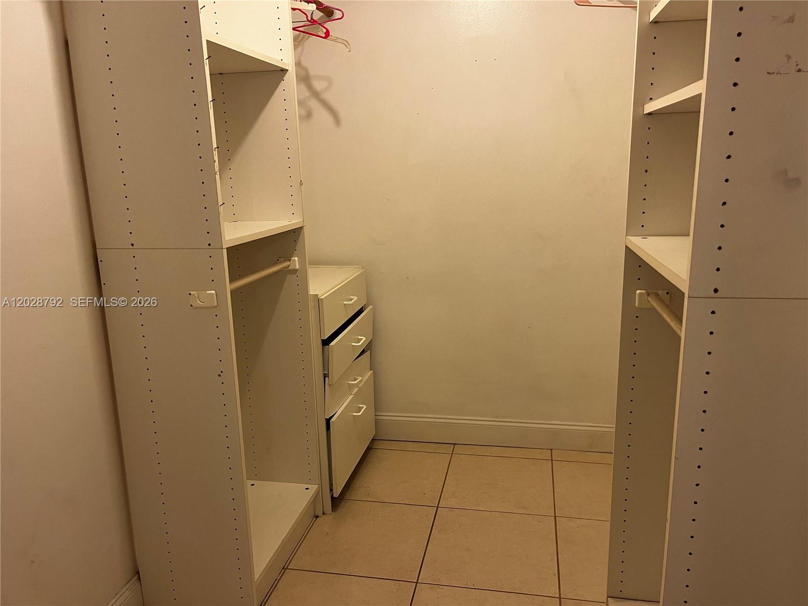 A walk-in closet features white modular shelving units, a small chest of drawers, and tile flooring — 7000 Nova Dr # 103E, Davie FL 33317, DAVIE, FL