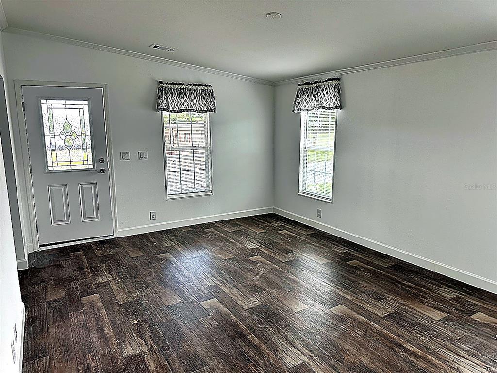 An empty room features light gray walls, dark wood-look flooring, and two windows with valances — 3496 GREENBLUFF ROAD UNIT 1118, ZELLWOOD, FL