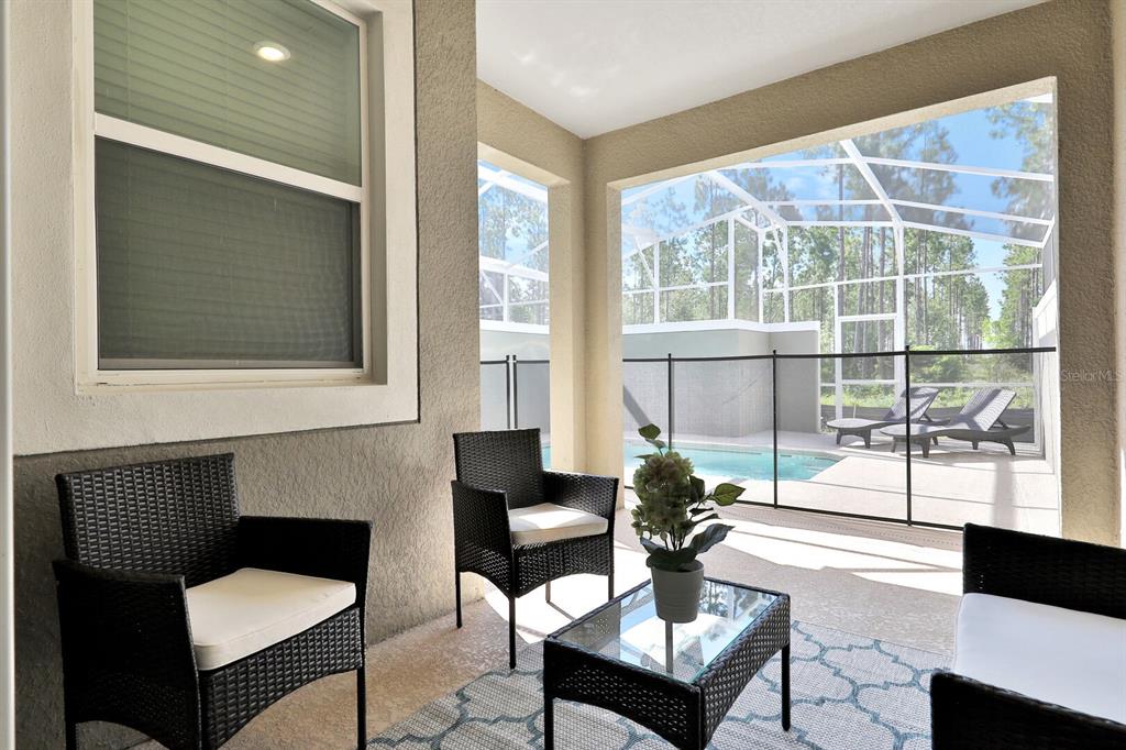 A covered patio features wicker chairs, a glass-top table, and a view of a screened pool — 392 OCEAN COURSE AVENUE, CHAMPIONS GATE, FL