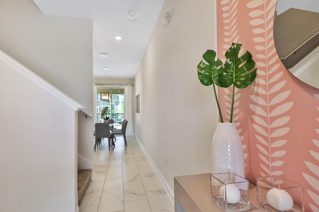 A hallway with tile floors leads to a dining area past a staircase and wallpaper — 392 OCEAN COURSE AVENUE, CHAMPIONS GATE, FL
