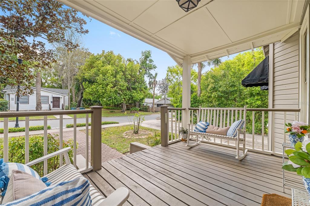A covered wooden porch features a rocking bench, striped cushions, and a view of the street — 721 SE 5TH STREET, OCALA, FL