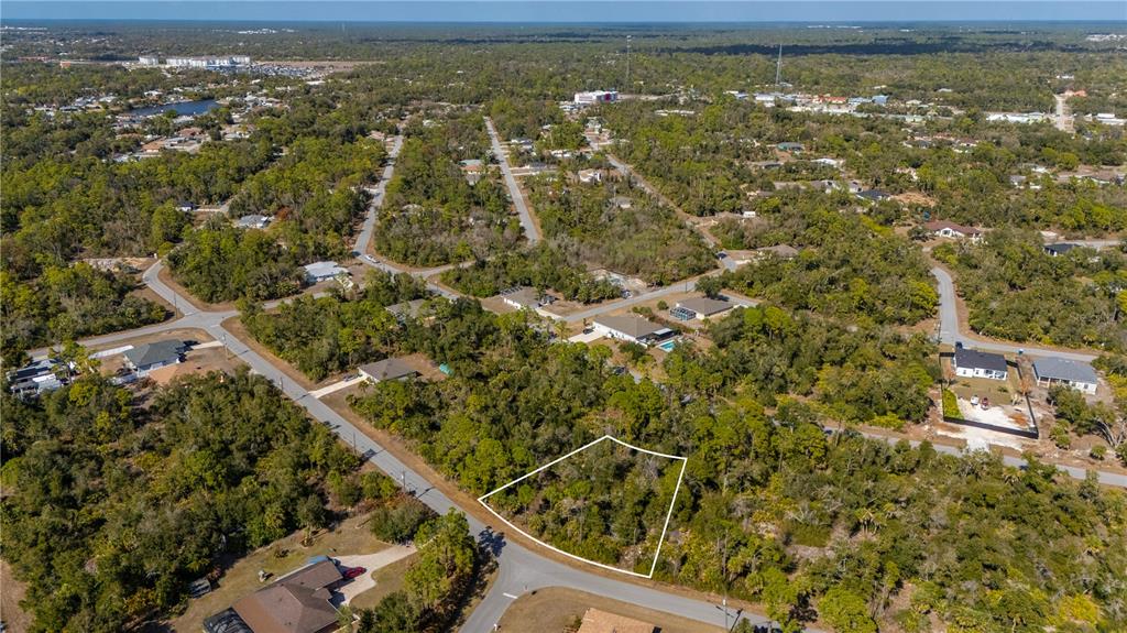 An aerial view shows a vacant, wooded residential lot outlined in white along a paved road — 1216 SHERWIN STREET, PORT CHARLOTTE, FL