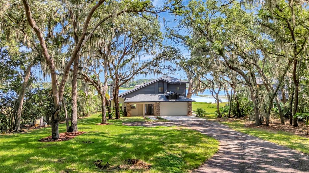 A two-story house with a garage sits on a grassy lot surrounded by mossy trees — 10547 LAKESHORE DRIVE, CLERMONT, FL