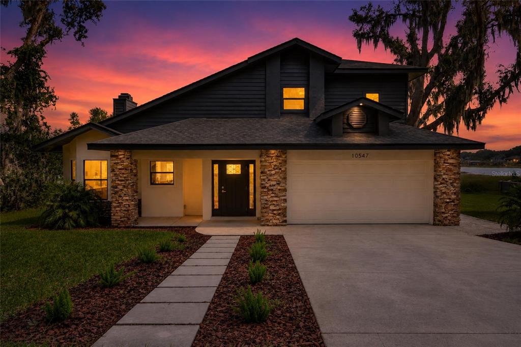 A two-story house with dark siding, stone accents, and a concrete driveway at sunset — 10547 LAKESHORE DRIVE, CLERMONT, FL