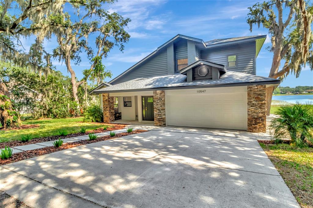 A two-story house with gray siding, stone accents, a two-car garage, and a concrete driveway — 10547 LAKESHORE DRIVE, CLERMONT, FL