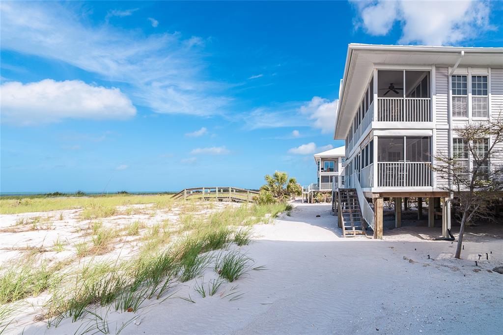 An elevated beach house with screened balconies sits on a sandy lot near the ocean — 7466 PALM ISLAND DRIVE UNIT 2913, PLACIDA, FL