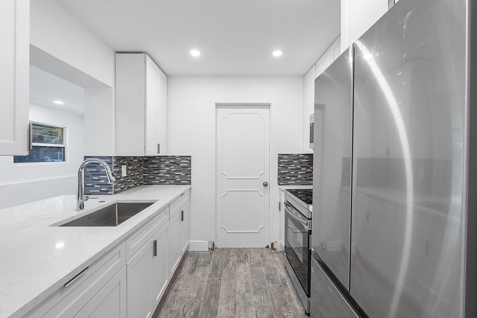 A modern kitchen features white cabinetry, quartz countertops, stainless steel appliances, and wood-look tile flooring — 370 S Golf Boulevard, Pompano Beach FL 33064, POMPANO BEACH, FL